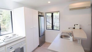 A compact kitchen with white cabinets, a stainless steel refrigerator, a built-in oven, a sink, and a window with a view of a deck.