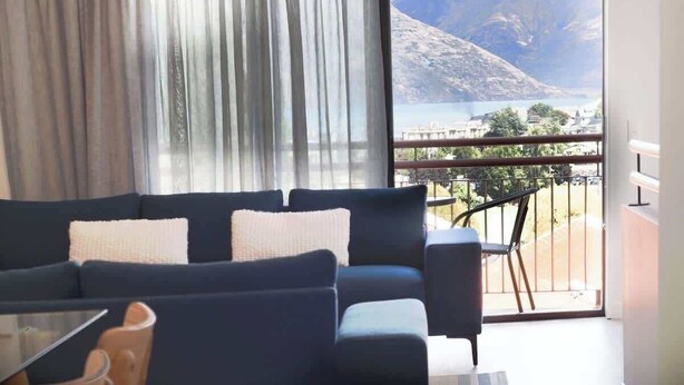 A living room with a sofa, a coffee table, and a view of mountains and a body of water through a balcony.
