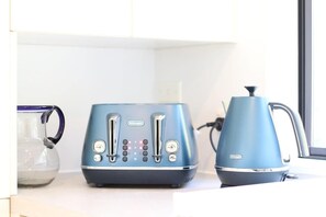 A kitchen with a blue toaster, a kettle, and a glass pitcher on the counter.