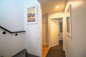 A staircase with a handrail, a door at the bottom, and a hallway leading to another room. - Central Qt - Lake Views - Hot Tub - King Bed (Queenstown)
