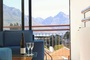 Varanda com vista para a montanha, uma mesa com garrafa e copo, e um sofá azul.