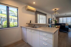 A modern kitchen with a built-in dishwasher, a sink, and a window with curtains. - Central Qt - Lake Views - Hot Tub - King Bed (Queenstown)