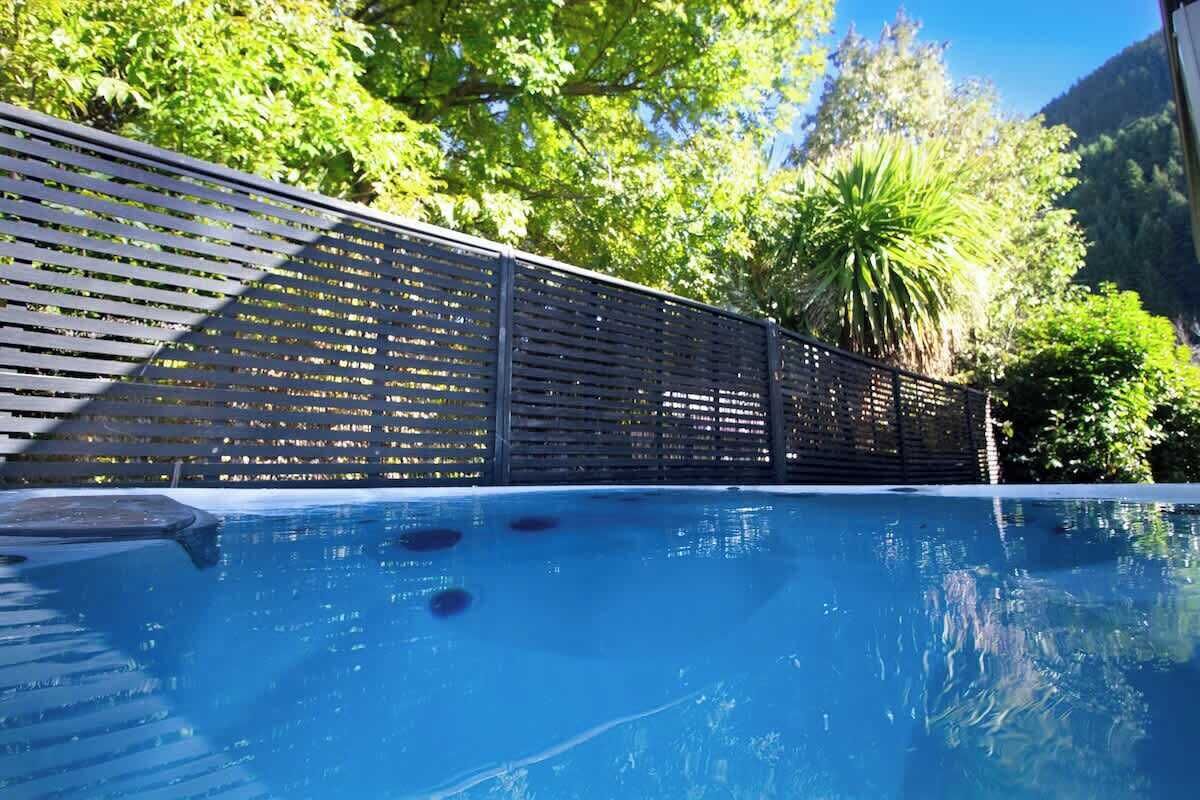 Une piscine entourée d’une clôture en bois, au milieu d’une végétation luxuriante et d’arbres.