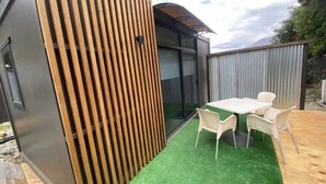 Un patio extérieur moderne avec une table et des chaises, un mur à lattes en bois et une zone recouverte de gazon synthétique vert.