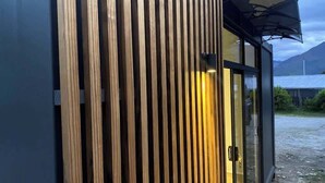 Un bâtiment doté de lambris en bois verticaux, d’une porte en verre et d’un auvent noir.