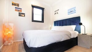 Une chambre à coucher avec un lit, une lampe de chevet, une fenêtre et des œuvres d’art murales.