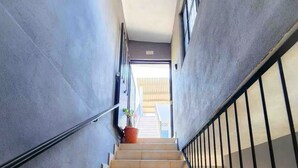Una escalera con peldaños color beige y barandillas negras que conduce a un espacio interior luminoso.
