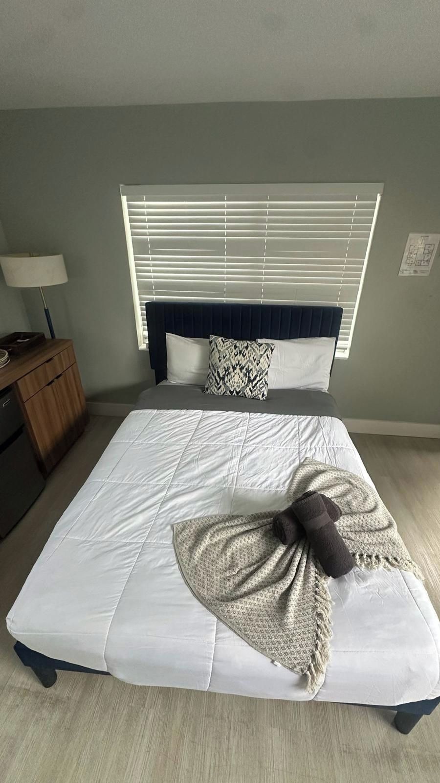 Un dormitorio con una cama, una mesita de noche, una lámpara y una ventana con persianas.