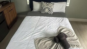 Un dormitorio con una cama, una mesita de noche, una lámpara y una ventana con persianas.