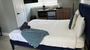Un dormitorio con cama, escritorio, silla, televisor y aire acondicionado.
