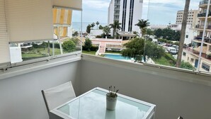 A balcony with a glass table and a potted plant, overlooking a pool and buildings with a prominent RIU sign. - Erisa 1, 47 - Studio with Terrace, Pool, Parking, 2nd line beach (Torremolinos)
