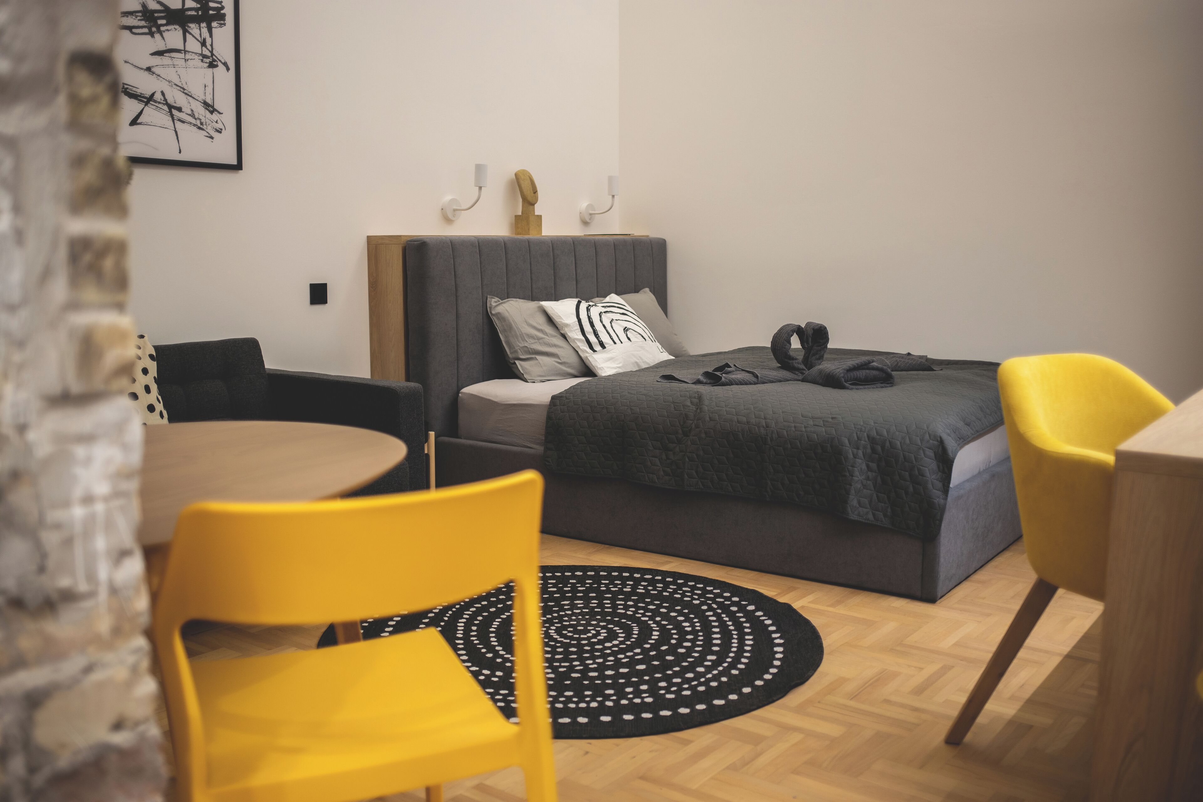 Un dormitorio moderno con una cama, una mesa de comedor redonda y una silla amarilla.