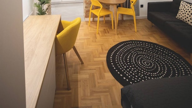 Eine moderne Wohnung mit freiliegenden Ziegelwänden, einer Küche mit weißen Schränken, einem Essbereich mit gelben Stühlen und einem Wohnzimmer mit einer schwarzen Couch.