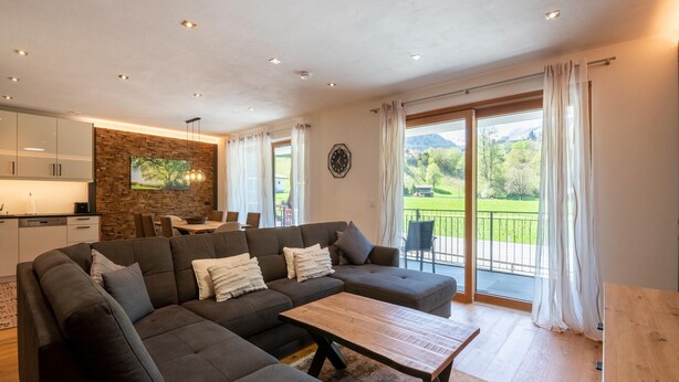 A modern living room with a sectional sofa, a wooden coffee table, and a dining area with a table and chairs. - Spacious Holiday Apartment Near Kitzbuhel (Jochberg)