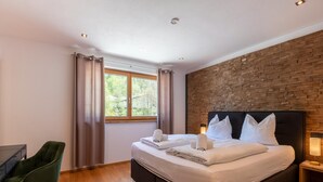 A modern bedroom with a large bed, a desk, and a view of greenery outside. - Spacious Holiday Apartment Near Kitzbuhel (Jochberg)