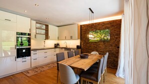 A modern kitchen with white cabinets, a wooden dining table, and a brick accent wall. - Spacious Holiday Apartment Near Kitzbuhel (Jochberg)