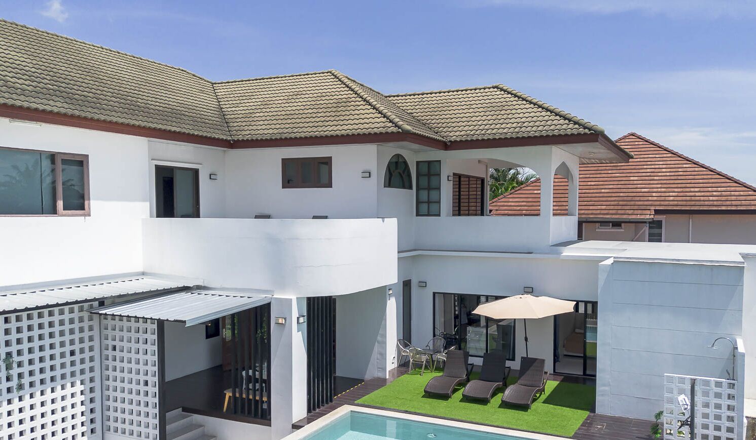 Ein modernes, zweistöckiges Haus mit Swimmingpool, Sitzgelegenheiten im Freien und einer überdachten Terrasse.