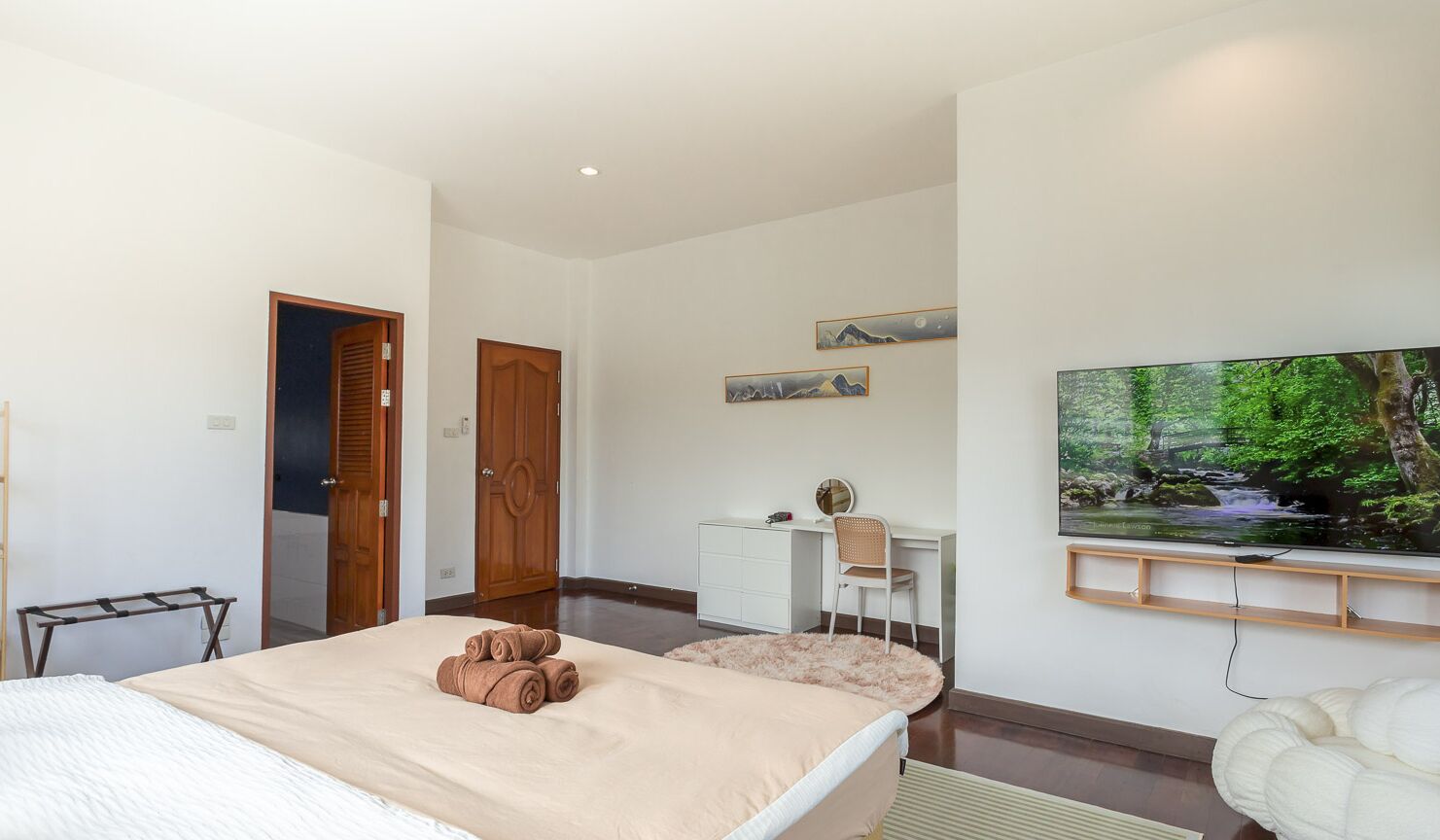 A bedroom with a bed, a desk, a chair, a TV, and a door.