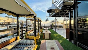 A rooftop terrace with seating areas, a small table, and a view of the cityscape. - The Hosteller Udaipur (Udaipur)