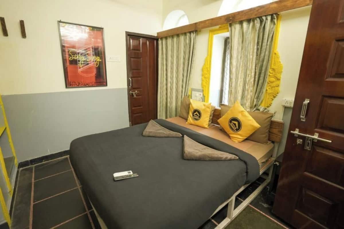 A single bed with a remote control, two yellow pillows, and a mirror above it.