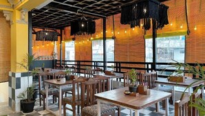 A restaurant with wooden tables and chairs, hanging black chandeliers, and brick walls. - The Hosteller Udaipur (Udaipur)