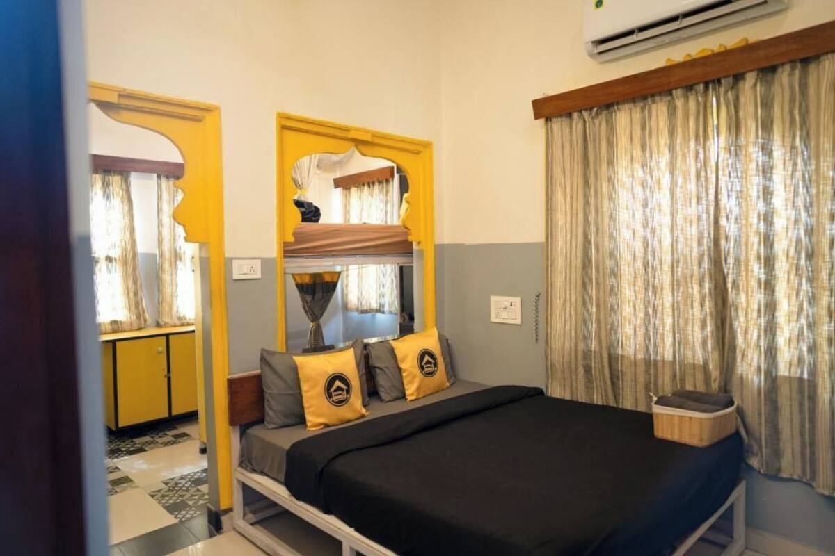 A bedroom with a bed, a mirror, a window with curtains, and a yellow cabinet.