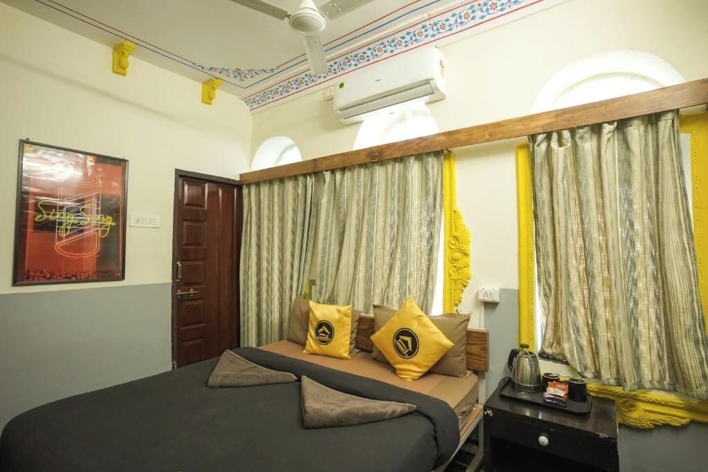 A hotel room with a bed, curtains, a wooden headboard, a nightstand, and a wall-mounted air conditioner.