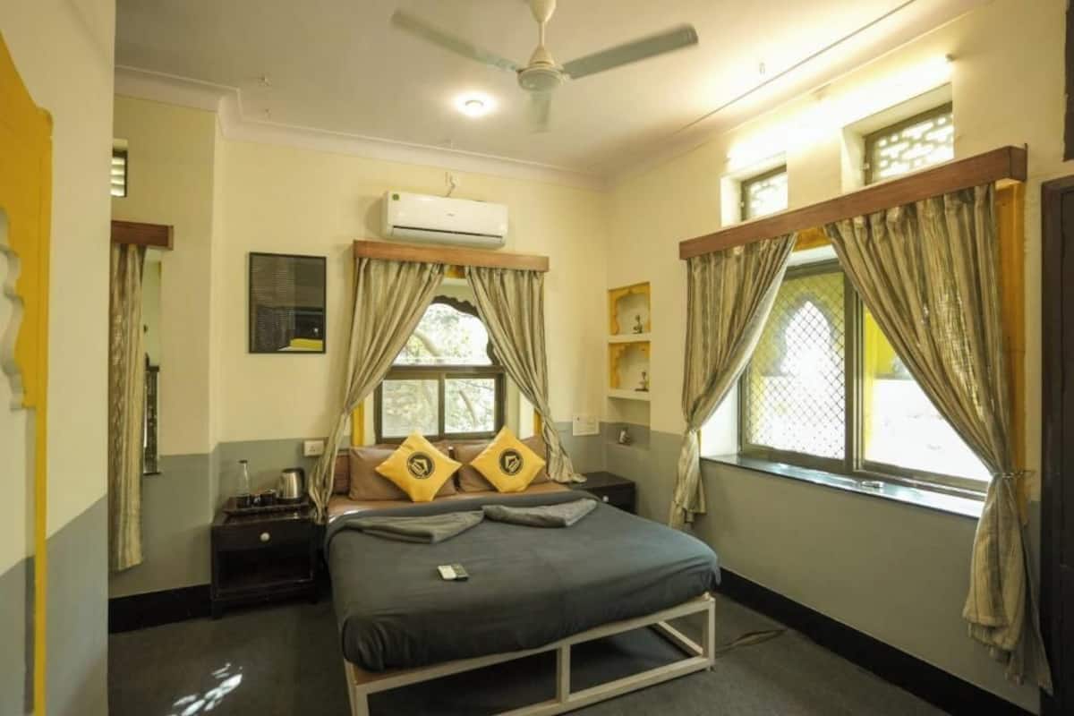 A bedroom with a bed, an air conditioning unit, a ceiling fan, and curtains.