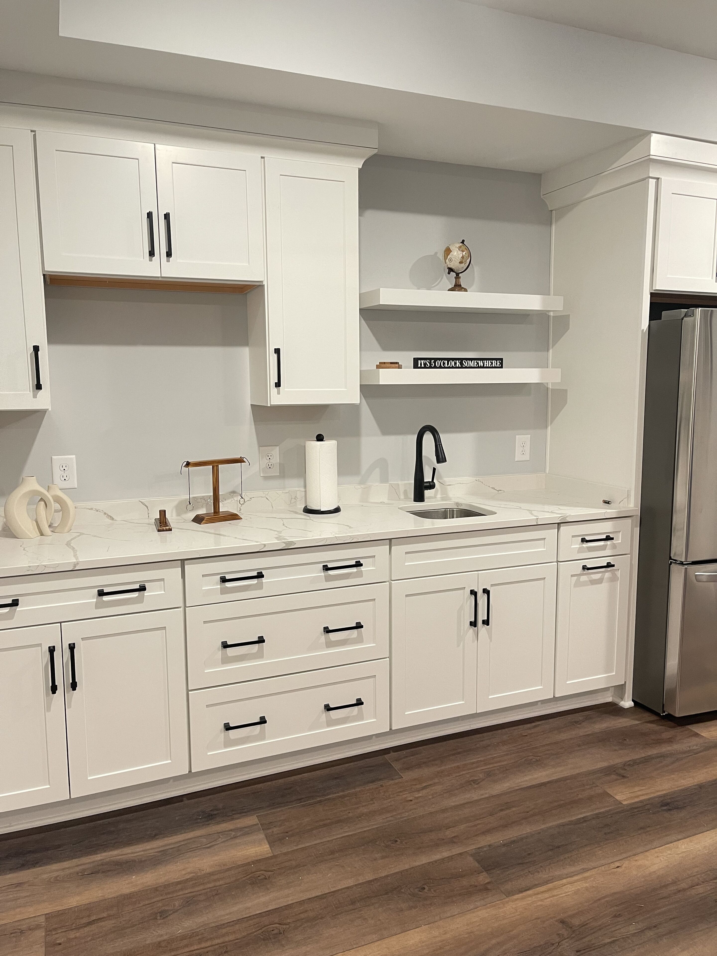 A modern kitchen with white cabinetry, a stainless steel refrigerator, and a marble countertop.