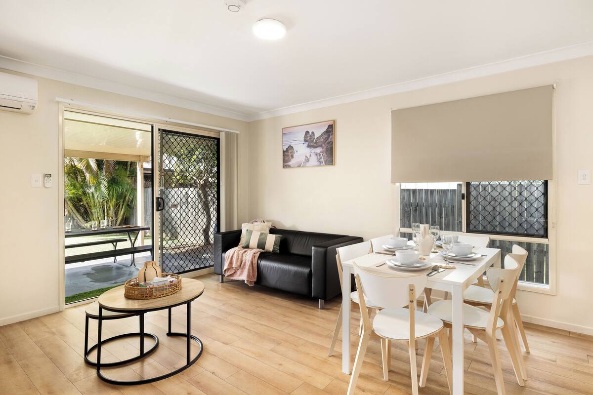 Una sala de estar moderna con comedor, un sofá de cuero negro, una mesita redonda y una mesa de comedor lista para cuatro comensales.