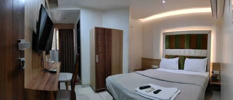 Habitación de hotel con cama, mesita de noche, televisor, armario y baño visible a través de una puerta.