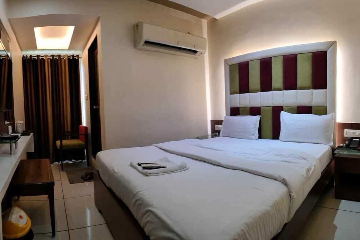A hotel room with a bed, a desk, a chair, an air conditioning unit, and a mirror.