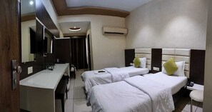 A hotel room with two beds, a desk, a mirror, and a bathroom. - Hotel Zenith Surat (Surat)