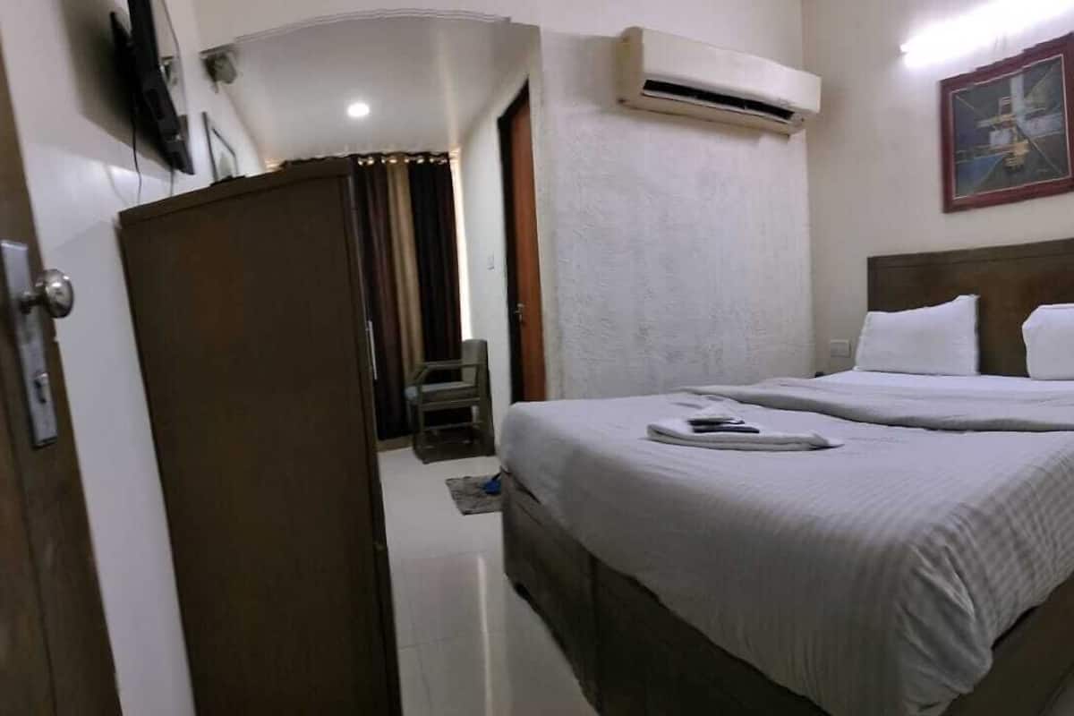 A hotel room with a bed, a nightstand, an air conditioning unit, and a door.