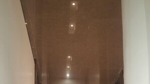 Un passadís modern amb un sòl reflectant, il·luminació empotrada i portes de fusta fosca.