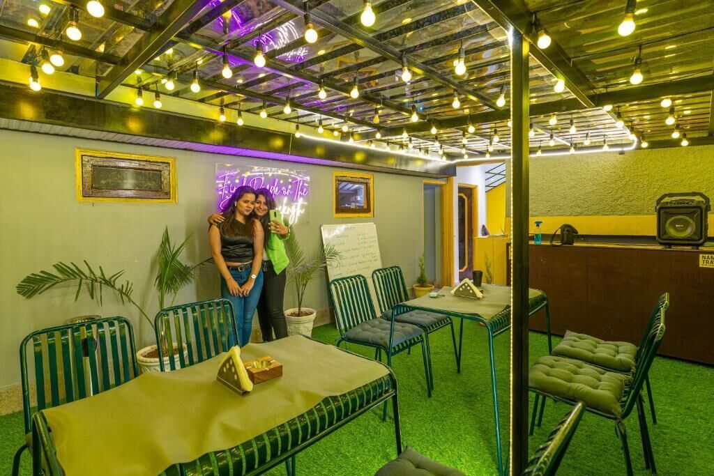 A room with green metal chairs, a table with a yellow tablecloth, and a neon sign on the wall.