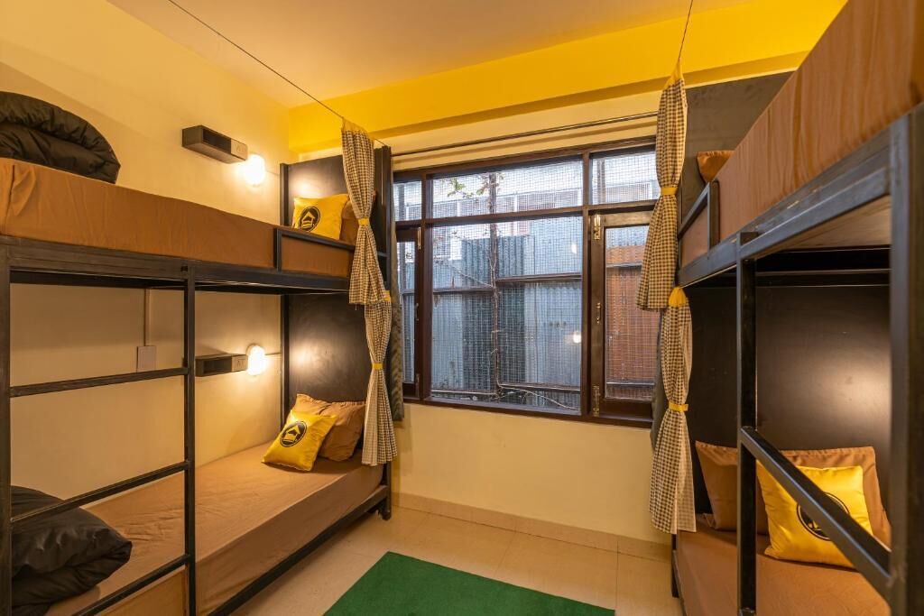 A dormitory room with bunk beds, a window with curtains, and a green rug.