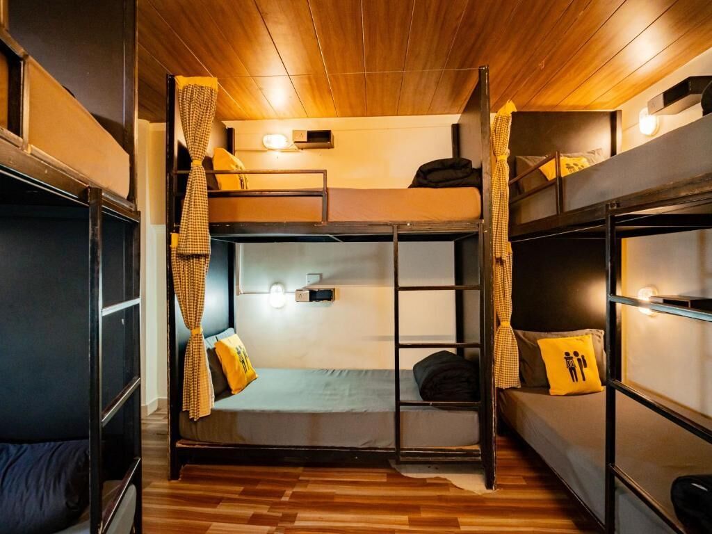 A bunk bed room with wooden flooring, a window, and a wall-mounted light fixture.