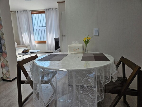 A dining area with a round table covered by a white tablecloth, surrounded by wooden chairs. - 3룸( Q,Q,SS) TOV 안정리게이트옆, 2층 조용한 주택가, long-term (Pyeongtaek)