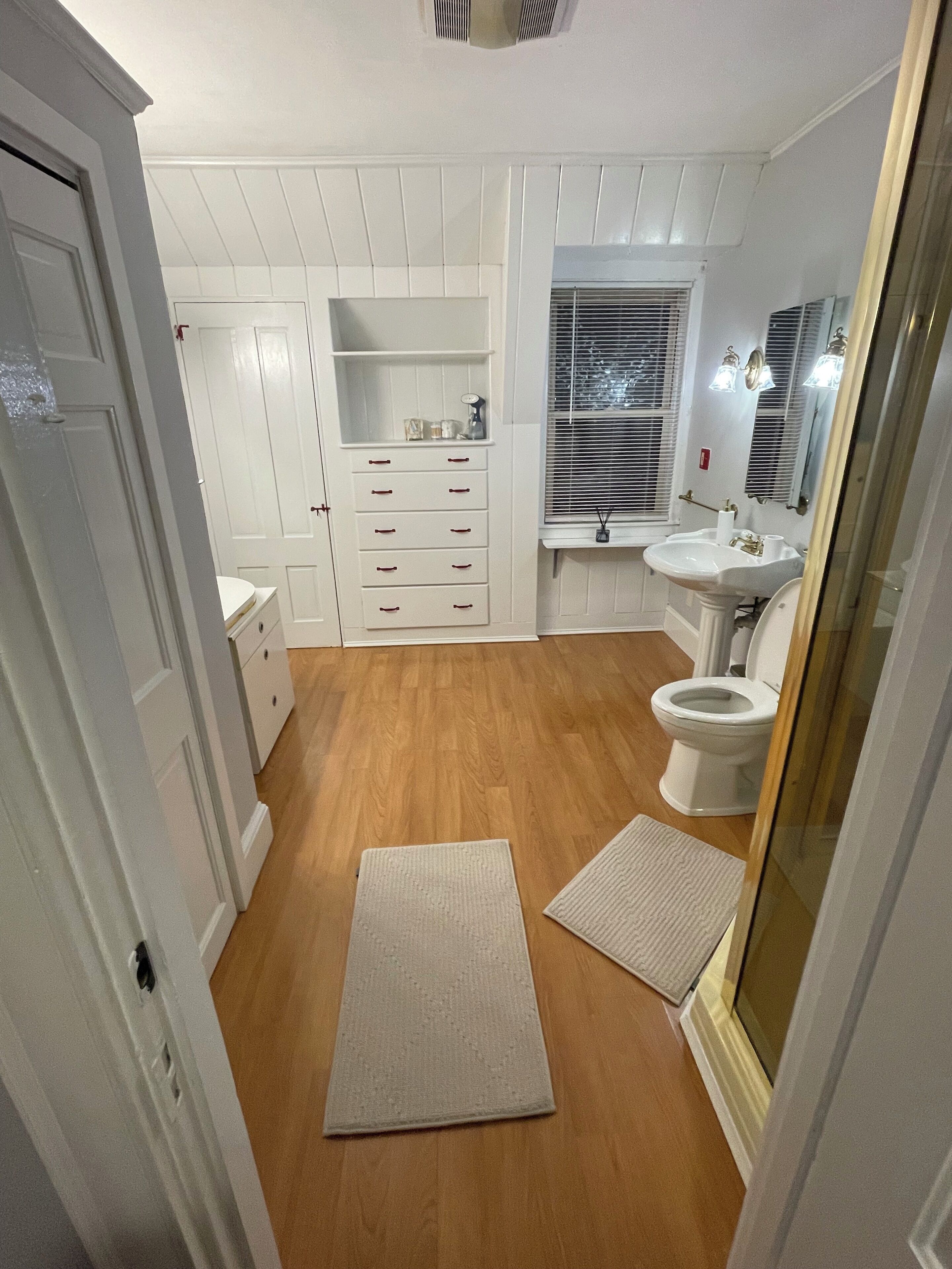 Une salle de bain avec un plancher en bois, des meubles blancs, un lavabo et des toilettes.
