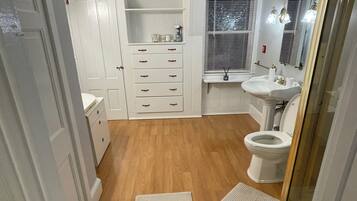 Une salle de bain avec un plancher en bois, des meubles blancs, un lavabo et des toilettes.