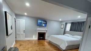 Un dormitorio moderno con una cama grande, una cama más pequeña, un televisor sobre la chimenea y una zona de estar con un banco.