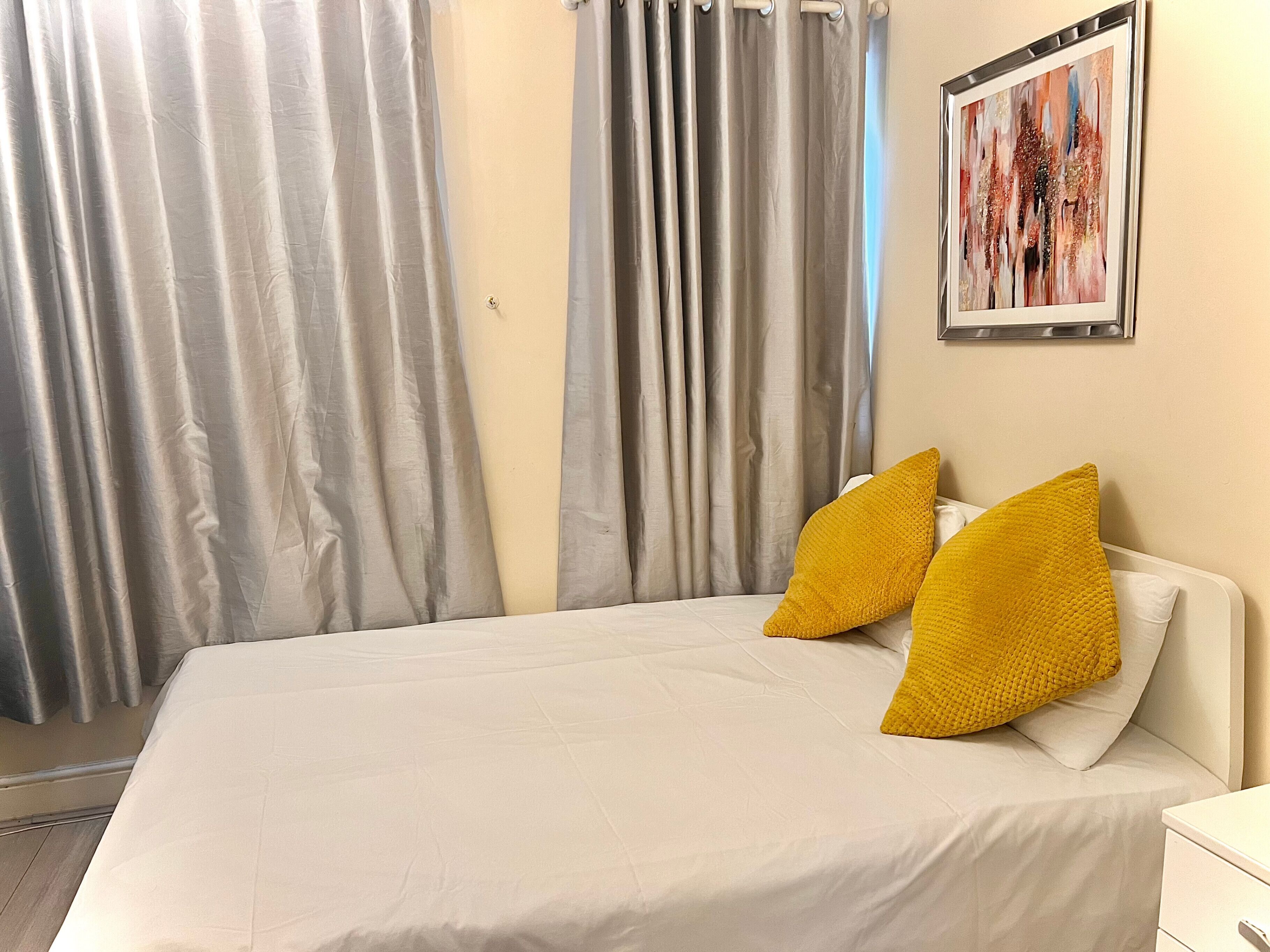 Ein Hotelzimmer mit Bett, Vorhängen, einem Gemälde und einem Nachttisch.