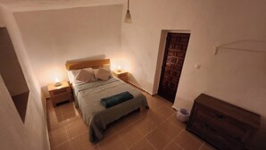 A bedroom with a bed, nightstands, a wall-mounted lamp, a wooden door, and a fireplace.