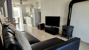 A living room with a black leather sofa, a flat-screen TV, a black entertainment unit, and a wood-burning stove.