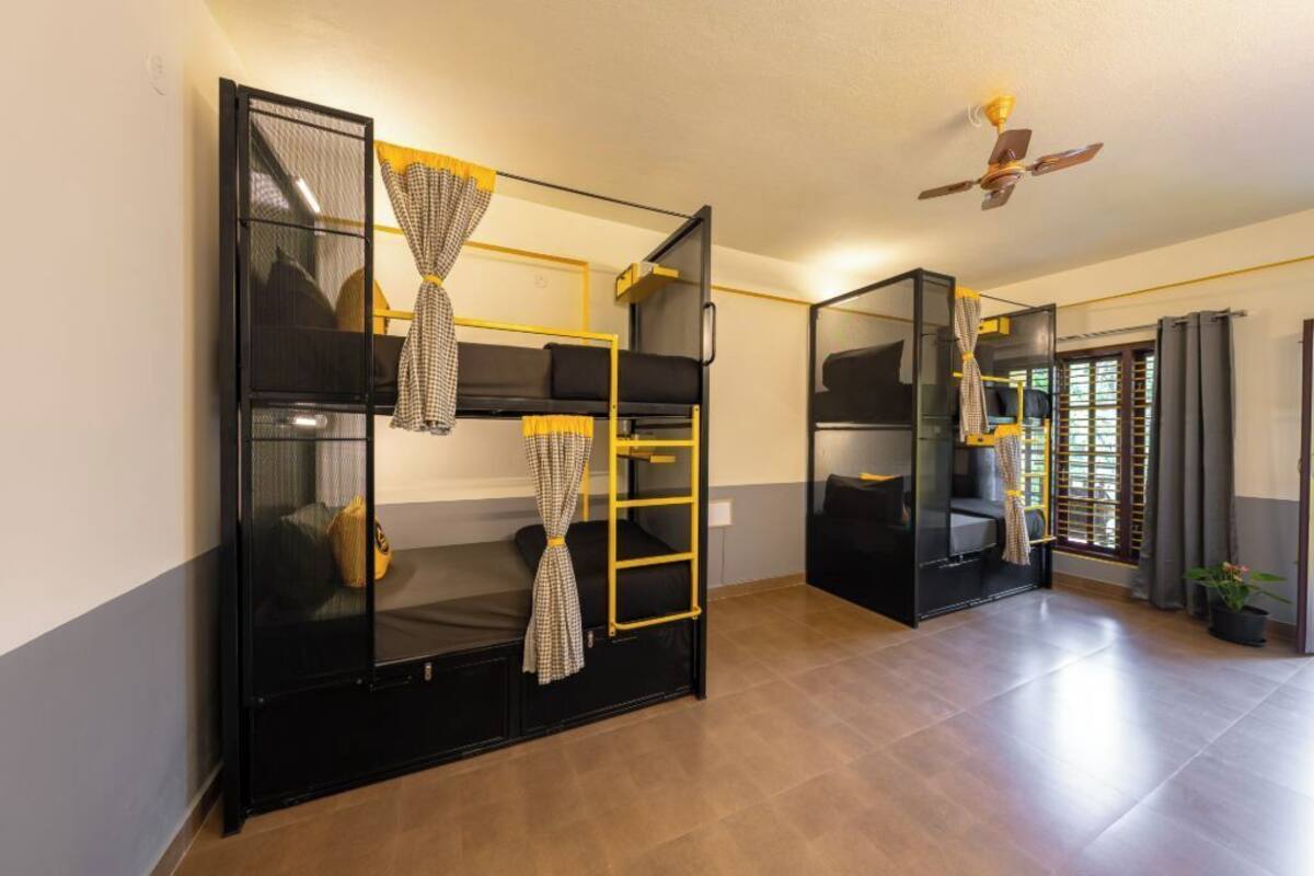 A room with bunk beds, a ceiling fan, and a window with curtains.