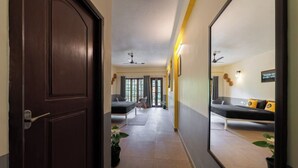 A hallway with a dark wooden door, a bed with a black mattress and white pillows, and a mirror reflecting the room. - The Hosteller Coorg Rainforest, Madikeri (Madikeri)