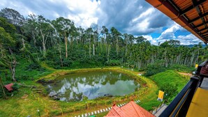 A view of a pond surrounded by lush greenery, a red-roofed building, and a yellow building in the foreground. - The Hosteller Coorg Rainforest, Madikeri (Madikeri)