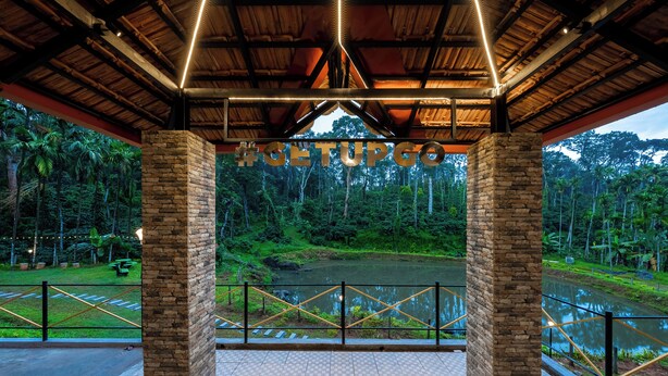 A covered pavilion with stone pillars, a view of a river, and a hashtag sign. - The Hosteller Coorg Rainforest, Madikeri (Madikeri)