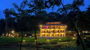 A two-story building with a balcony, surrounded by greenery and a body of water. - The Hosteller Coorg Rainforest, Madikeri (Madikeri)